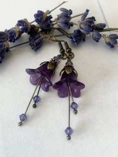 two purple flowers are hanging from some kind of hook - on earwires with tiny beads