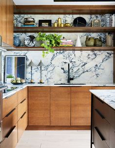 a kitchen with marble counter tops and wooden cabinets, along with shelves filled with plants