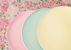 three plates with different colors are sitting on a floral tablecloth, one is blue and the other is pink