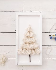 a small white christmas tree in a frame on a wooden wall next to scissors and yarn