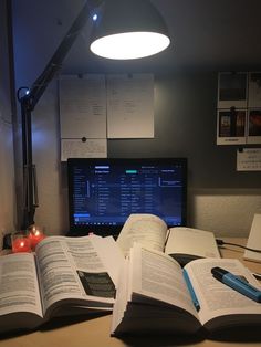 an open book sitting on top of a desk next to a computer monitor and lamp