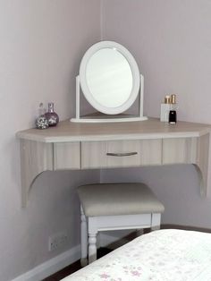 a white dressing table with a stool and mirror on it's top, next to a bed