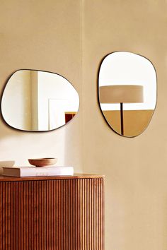 two round mirrors are hanging on the wall above a wooden cabinet and table with a lamp