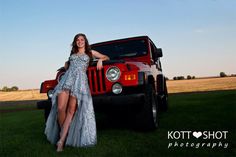 a woman standing next to a red jeep on top of a lush green grass covered field