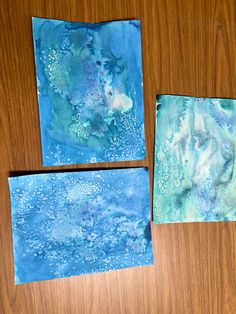 three pieces of blue and green art work on a wooden table with one piece cut out