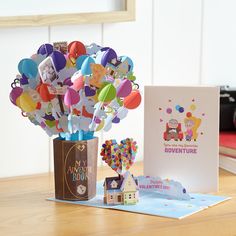 a vase filled with lots of balloons next to a greeting card and an open book