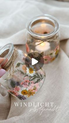 a person holding a glass jar filled with flowers on top of a white table cloth