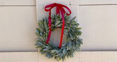 a wreath hanging on the side of a white building with a red ribbon around it