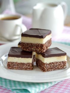 four pieces of dessert sitting on top of a white plate next to a cup of coffee