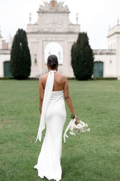 a woman in a white dress is walking through the grass with her back to the camera