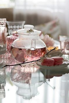 a glass table topped with pink macaroons and teapot filled with liquid sitting on top of it