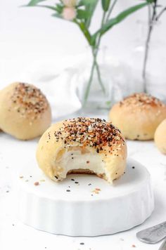 three bagels with poppy seed sprinkles on a white plate next to a flower vase