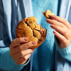 a woman holding a cookie in her hands and looking at it with one bite taken out