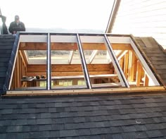 two men are standing on the roof of a house that is being built with wood shingles