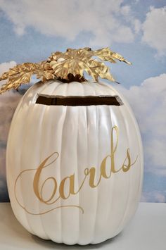 a white pumpkin decorated with gold leaves and the word cards painted on it's side