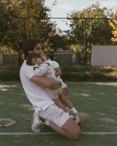 a man holding a baby while sitting on top of a tennis court