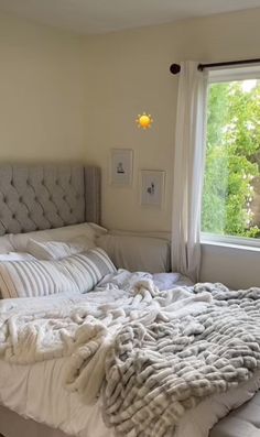 an unmade bed sitting in front of a window next to a white blanket and pillows