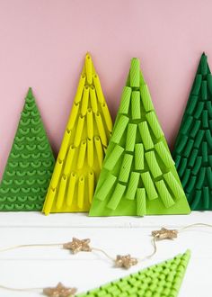 three paper christmas trees sitting next to each other on a white table with pink background