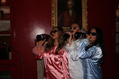 two women taking pictures with their cameras in front of a red wall and painting on the wall