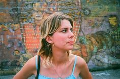 a woman standing in front of a wall with graffiti on it's walls and looking off into the distance