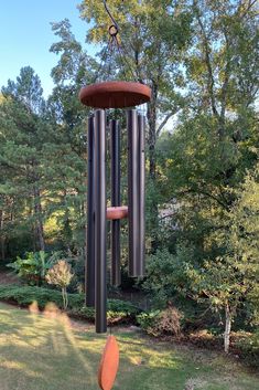 a wind chime in the middle of a yard with trees and bushes behind it