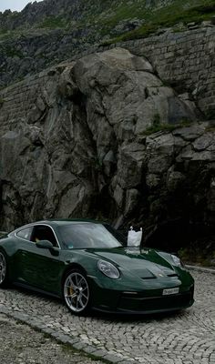 a green sports car parked in front of a rocky mountain side with a white cat sitting on top of it