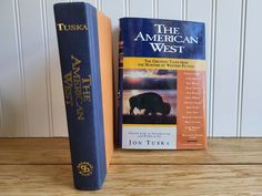 two books sitting next to each other on top of a wooden table in front of a white wall