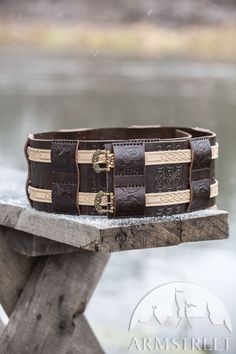 a close up of a leather bracelet on a wooden bench near the water and trees