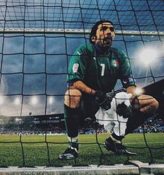 a man sitting in front of a soccer net with his feet on the goalie's knee