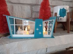 candles are lit in front of a window on a mantle with red and white decorations