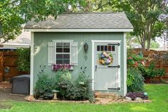 a garden shed with flowers and plants in the front yard, next to a fence