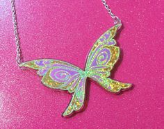 a necklace with a colorful butterfly on it sitting on a pink surface, in front of a chain