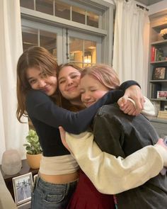 three girls hugging each other in front of a window