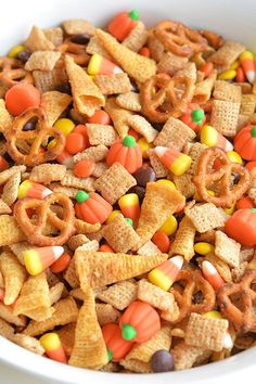 the cereal mix is being poured into a bowl with candy corn and pretzels