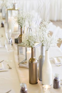 the table is set with white flowers and silver vases