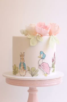 a white cake with pink flowers on top and an image of peter rabbit on the side