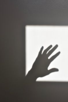 the shadow of a person's hand on a white wall with a square light box in the background