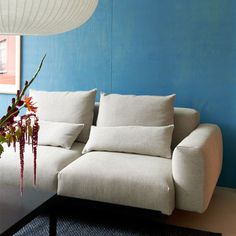 a white couch sitting in front of a blue wall next to a vase with flowers