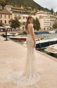 a woman in a long dress standing on a dock next to some boats and buildings