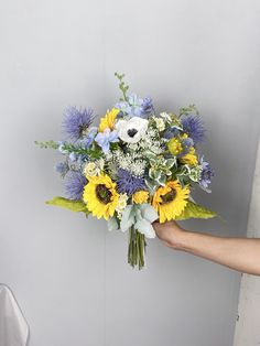 a person holding a bouquet of flowers in their left hand, with blue and yellow colors