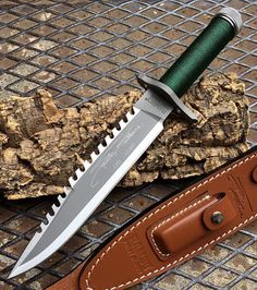 a knife with a green handle sitting on top of a piece of wood next to a brown leather sheath