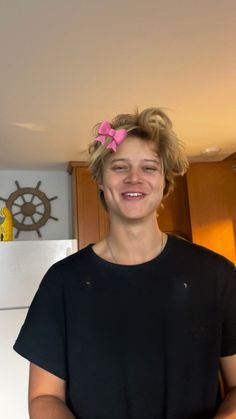 a woman standing in a kitchen wearing a black shirt with a pink bow on her head