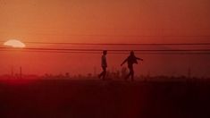 two people walking across a field under power lines at sunset with the sun in the background