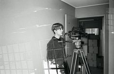 a young man standing in front of a camera on a tripod next to a wall