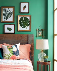 a bedroom with green walls and pictures on the wall above the bed, along with a lamp