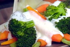 broccoli and carrots are covered in white sauce