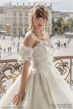 a woman in a white wedding dress posing for a photo on a balcony overlooking the city