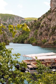 two boats are docked in the water near some cliffs and trees, with one boat on it's side