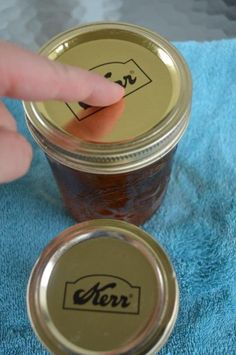 a person pointing at a jar with jam in it on a blue towel next to another jar