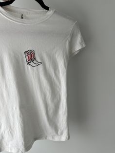 a white t - shirt with a red and black embroidered boot on the front, hanging from a hanger